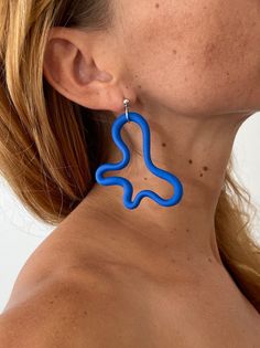 a close up of a person wearing large blue earring with wavy lines on them