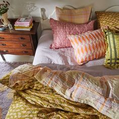 a bed topped with lots of pillows next to a night stand filled with books and flowers