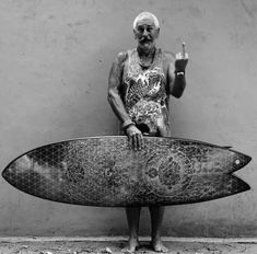 an old man holding a surfboard in front of a wall