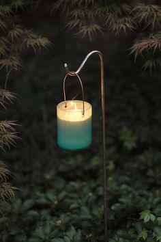 a lit candle sitting on top of a metal pole in the middle of some bushes