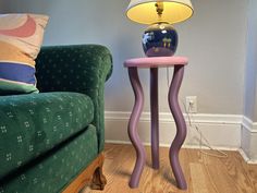 a lamp sitting on top of a pink table next to a green couch in a living room