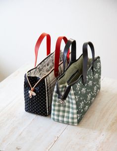 two purses sitting on top of a wooden table next to each other with handles