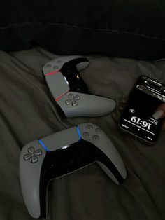 two nintendo wii game controllers sitting on top of a bed next to a cell phone