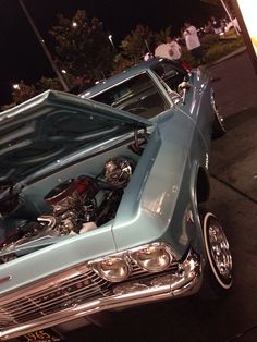 an old blue car with the hood up and engine in it's trunk at night