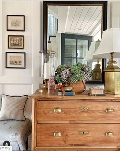 a wooden dresser topped with a mirror next to a lamp and pictures on the wall