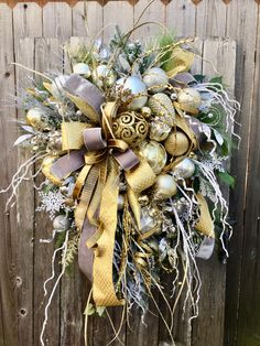 a wreath is hanging on the side of a wooden fence, decorated with gold and silver ornaments