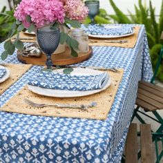 a blue and white table cloth with pink flowers in a vase sitting on top of it