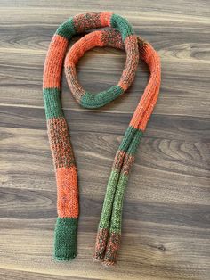 an orange and green knitted scarf laying on top of a wooden floor next to a pair of scissors