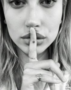 black and white photograph of a woman making a hush sign with her finger in front of her mouth