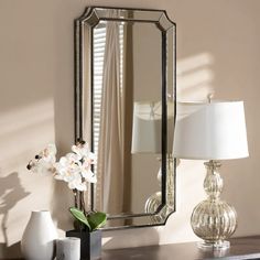 a mirror sitting on top of a table next to a lamp and vase with flowers