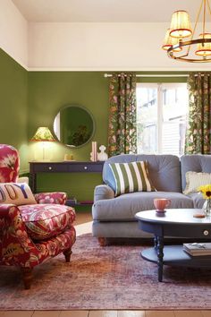 a living room with green walls and furniture in the center, along with floral curtains