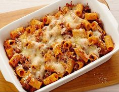 a casserole dish filled with pasta and meat in a white baking dish on top of a wooden table