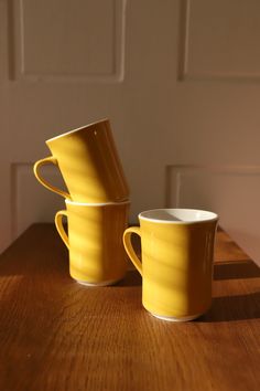 three yellow cups sitting on top of a wooden table