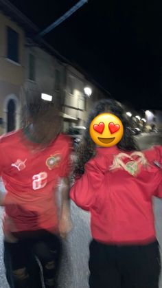 two people in red shirts with faces painted on them walking down the street at night