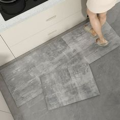 a woman standing in front of a stove top oven next to a rug on the floor