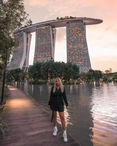 a woman standing on a dock in front of some tall buildings with water and trees