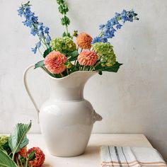 a white vase filled with lots of flowers on top of a table next to napkins