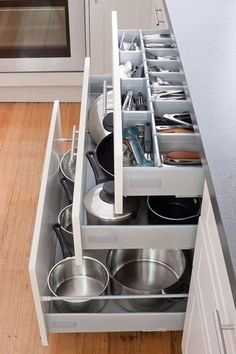 an open drawer in a kitchen filled with pots and pans on top of wooden floors