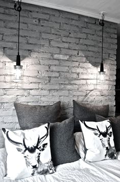 a bed with three pillows and two lights on the headboard, in front of a brick wall