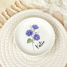 a white plate topped with purple flowers on top of a doily covered place mat