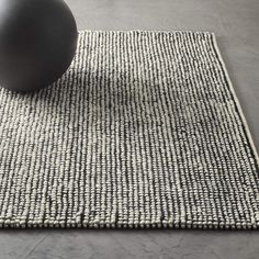 a gray ball sitting on top of a rug next to a black object in the middle