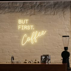 a neon sign that reads, but first coffee on the side of a brick wall