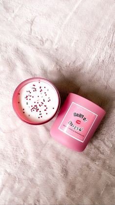 a pink candle sitting on top of a white bed next to a bowl with sprinkles