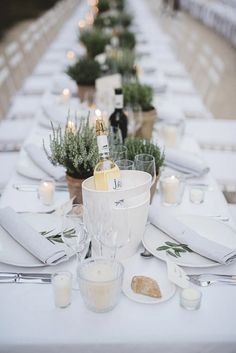 a long table is set with white linens and silverware for an elegant dinner