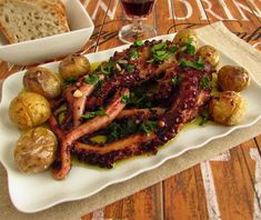 an octopus dish on a plate with potatoes, bread and red wine in the background