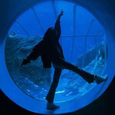 a person standing in front of an aquarium looking at the water and holding their arms up