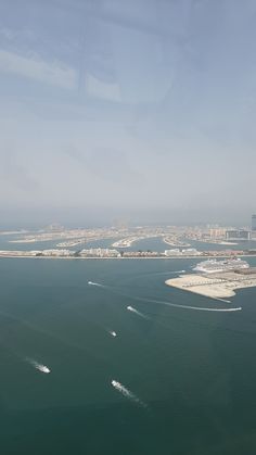 an airplane flying over the ocean with boats in the water and buildings in the background