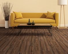 a living room with wood flooring and yellow couch in the center, two vases on coffee table