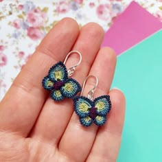 small crocheted butterfly earrings in blue and yellow colors on a hand - held background