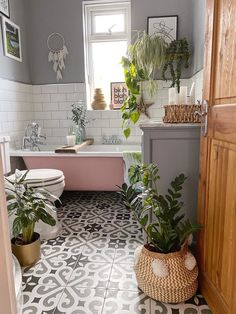 two potted plants sit on the floor in front of a bathtub and toilet