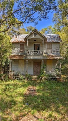 an old run down house in the middle of some trees and grass with a porch