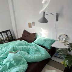 an unmade bed with green sheets and pillows in a white room next to a lamp