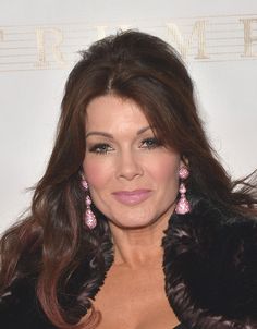 a woman with long brown hair and pink earrings posing for a photo on the red carpet