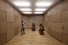 three cello players are playing in an empty room with wood paneling on the walls