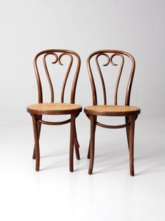 two wooden chairs sitting next to each other on a white surface with one chair facing the camera