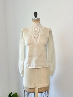 1970s Gunne Sax sheer cotton ivory long sleeve blouse with button down closure down the back middle. This shirt has a gorgeous floral lace mock neck that continues down the front middle.  In very good vintage condition, minor discoloration by armpit it hardly noticeable! B: 34" W: 31" L: 22" Vintage Beige Blouse For Spring, Vintage Long Sleeve Sheer Tops, Vintage White Blouse For Spring, Vintage Fashion Lace Collar Long Sleeve Blouse, Vintage Fashion Long Sleeve Blouse With Lace Collar, Vintage Long Sleeve Blouse With Lace Collar, Vintage White Long Sleeve Top With Lace Trim, Vintage Sheer Blouse For Spring, Vintage Long Sleeve Blouse With Lace Trim