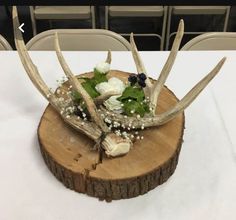 an arrangement of flowers and antlers on a wooden slice at a wedding reception table