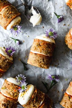 carrot rolls with cream cheese frosting and purple flowers on top, surrounded by spoons