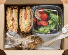 an open lunch box with sandwich, salad and fork