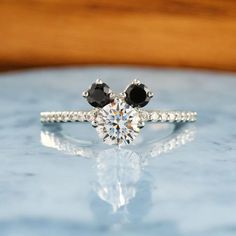 an engagement ring with two black and white stones on the side, sitting on top of a table