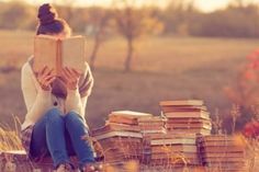 a woman sitting on the ground reading a book with stacks of books in front of her