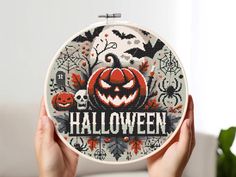 someone is holding up a cross stitch halloween pattern in front of a white background with black and orange pumpkins