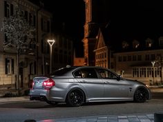 a silver car is parked on the side of the road at night with buildings in the background