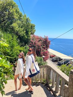 two women walking up some steps near the ocean and trees with their backs to each other