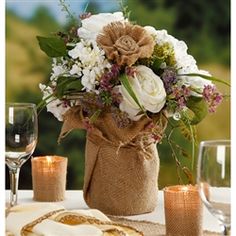 the table is set with wine glasses, napkins and flowers in burlap bags