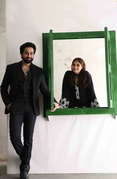 a man standing next to a woman in front of a green framed photo on the wall